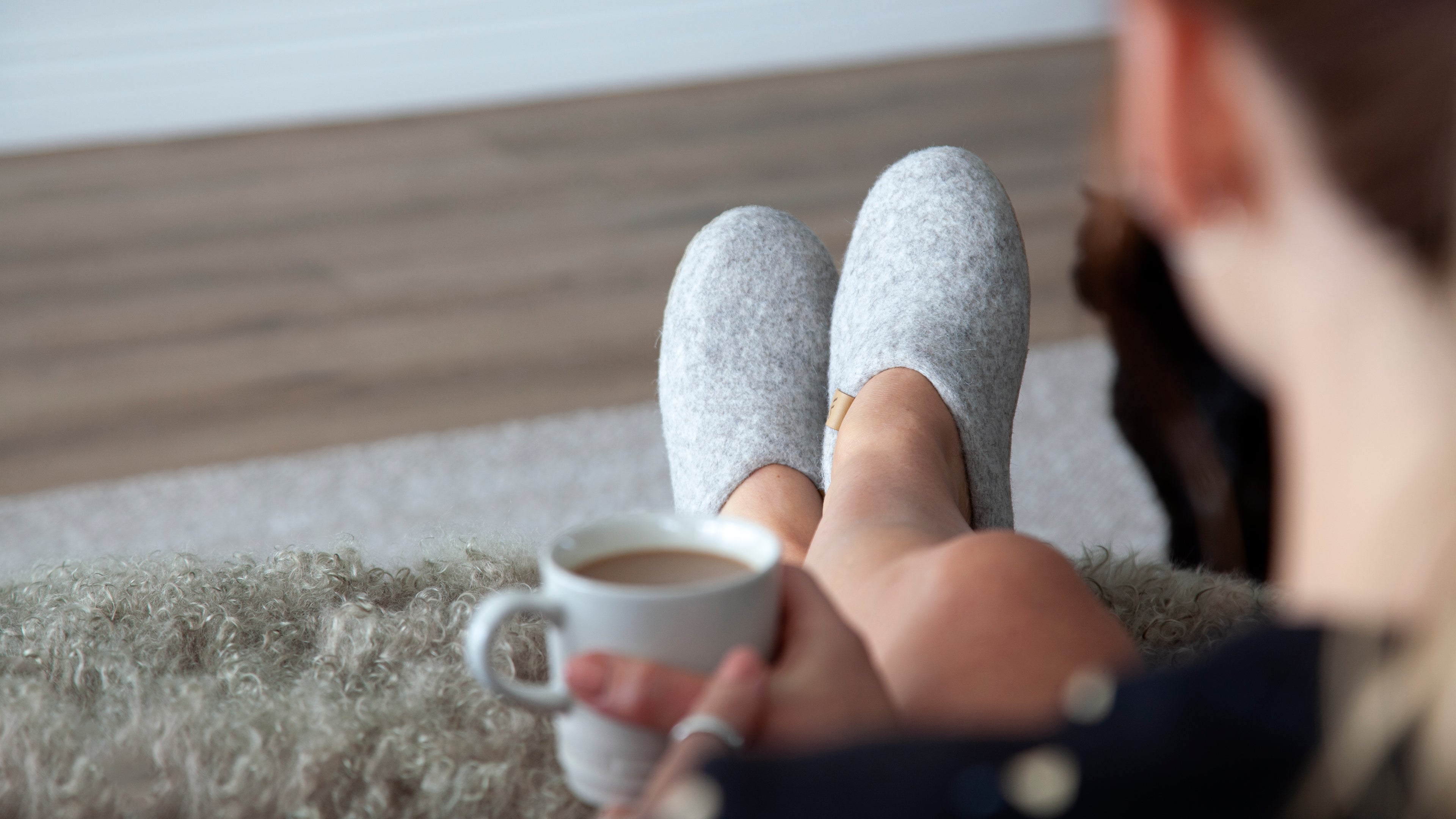 Woman wearing grey slip on new Zealand Wool Slippers while drinking coffee